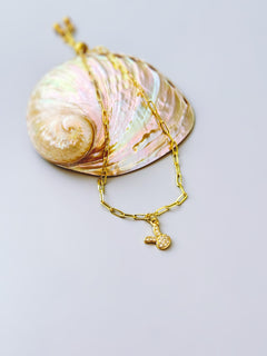 May include: A gold-colored necklace with a small bunny pendant. The necklace is made of a chain link design. The pendant is a small bunny with a textured surface. The necklace is resting on a large, iridescent seashell.